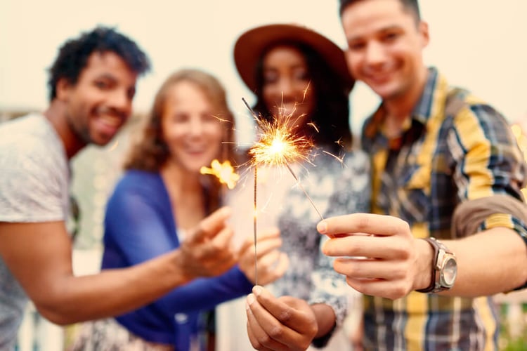 Multi-ethnic millenial group of friendsfolding sparklers on rooftop terrasse at sunset-1_seo-opt
