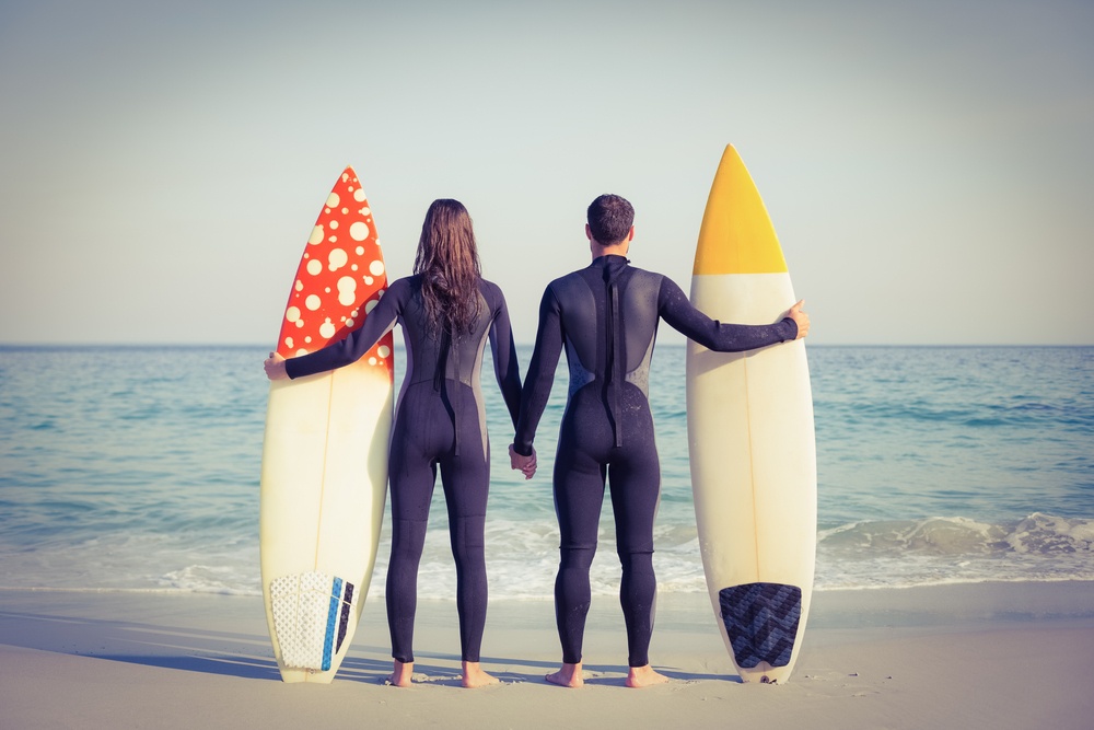 happy couple in wetsuits with surfboard on a sunny day