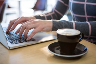 Mid section of woman using laptop with coffee on table in cafeteria_seo-opt-1-1