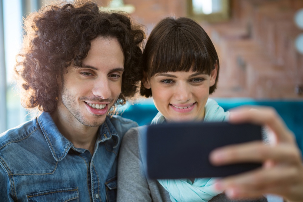Smiling couple taking selfie on mobile phone in cafeteria